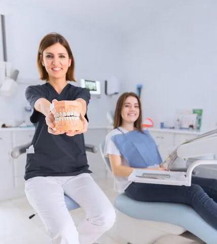 smiling female dentist showing teeth sitting behind patient in dental clinic