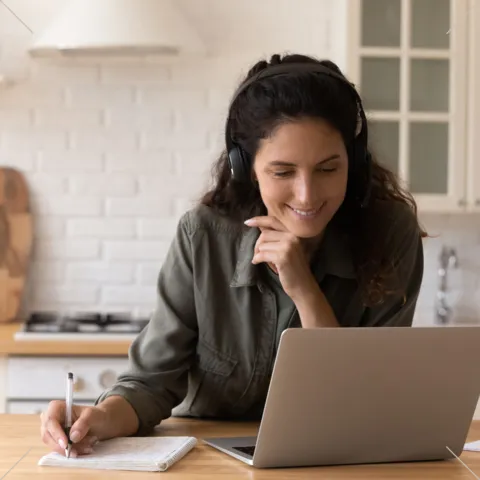 smiling woman looking at computer, taking notes