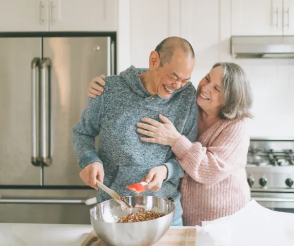 woman and man embracing and smiling while cooking in kitchen