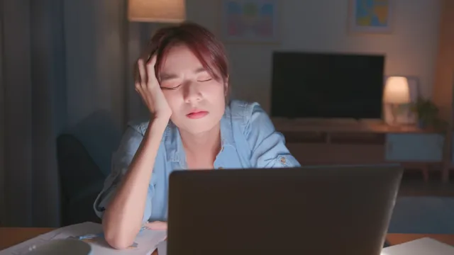 Tired woman sitting in front of laptop at night with eyes closed