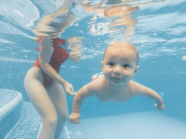 Happy Infant playing in the water holding his breathe - Baby Swimming Lessons Singapore