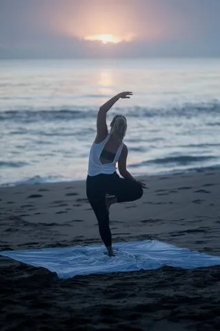 Woman doing yoga on the beach facing the yoga in a standing pose