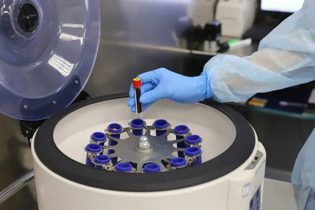 A nurse in blue latex gloves performs a blood analysis in centrifuge