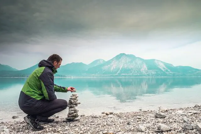 man stacking rocks next to mountain lake