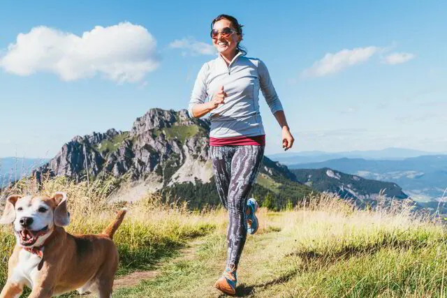 woman running with dog on grassy ridge