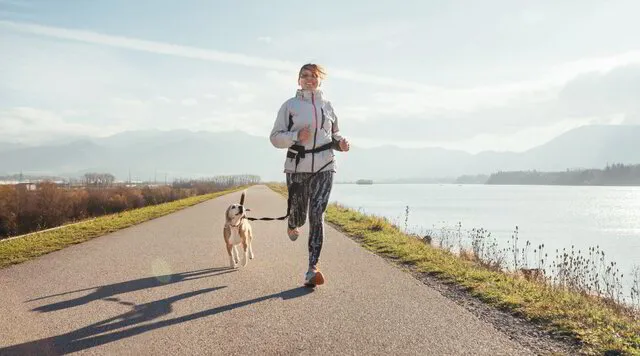 woman running with dog beside lake