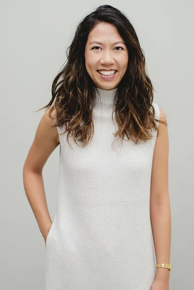 Dr. Emma Lee, ND with wavy hair in a white sleeveless dress against a grey background.