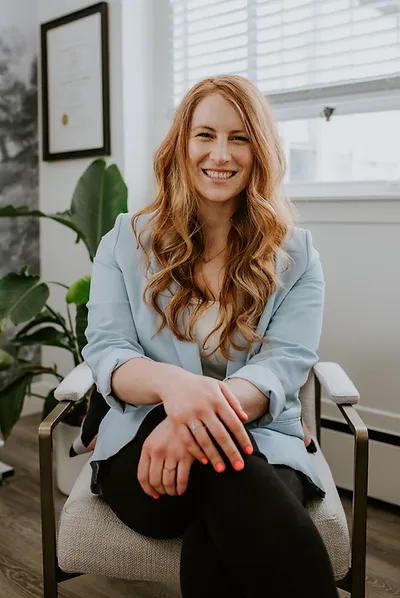 Dr. Jessalyn Shamess, ND in blue blazer sitting in an office chair with a plant in the background.