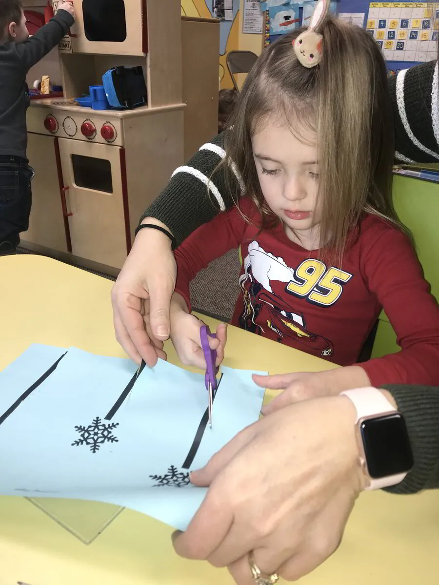 child cutting paper with scissor with adult helping at Discovery Christian Preschool in Effingham IL