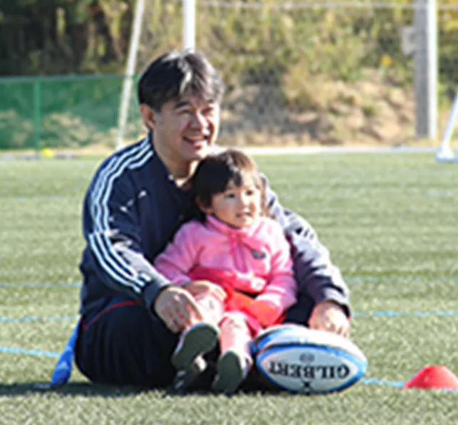 子どもとラグビーボールを囲む山羽教文