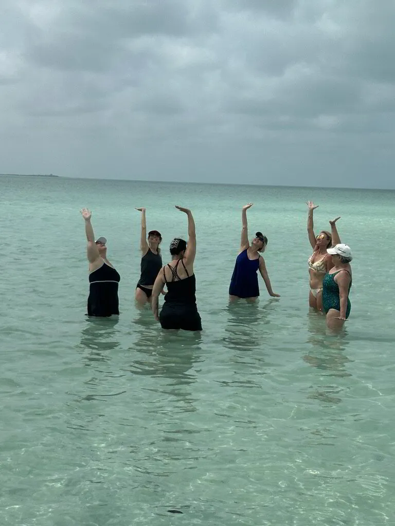 Participants gather in a circle and excitedly raises their hands in the water.