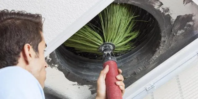A man putting a duct cleaning brush up a large vent
