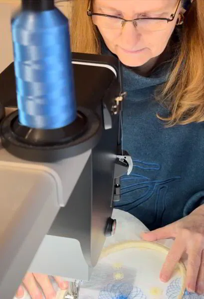 Jacqueline Steudler concentrating while using a sewing machine to embroider water soluble fabric with a floral design.