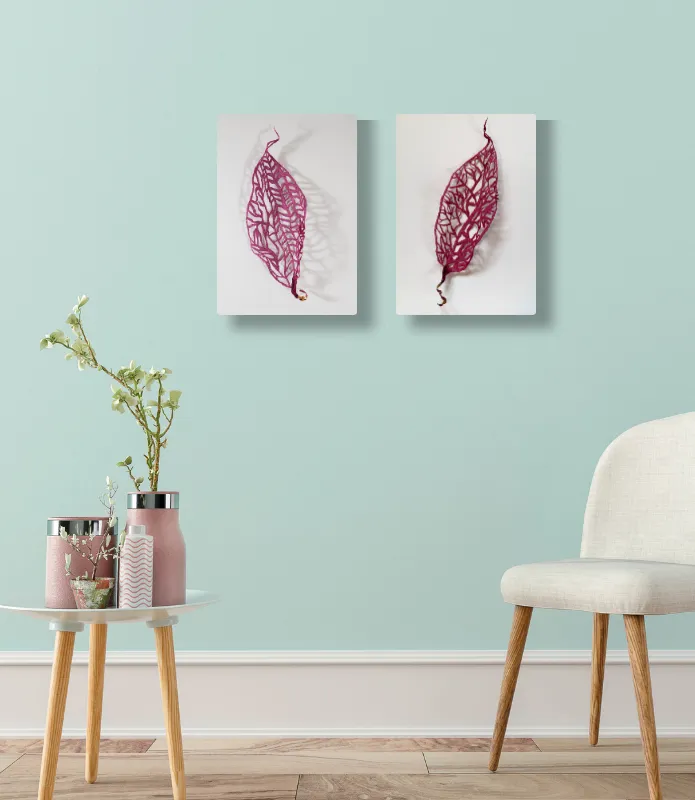 A modern living space featuring two framed seed pod thread sculptures by Jacqueline Steudler  on a pastel wall, a glass side table with a potted plant and candles, and a white chair.