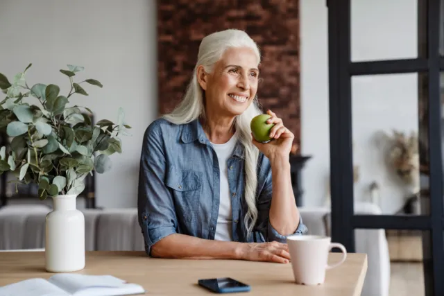 Woman sitting at kitchen table eating a green apple