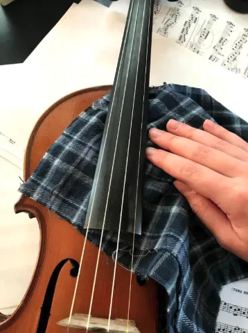 A person wiping down underneath the fingerboard on the violin with a cloth.
