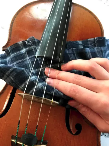 A person wiping down the violin body underneath the strings, where the rosin builds up.
