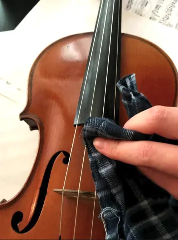 A person wiping down violin strings with a cloth.