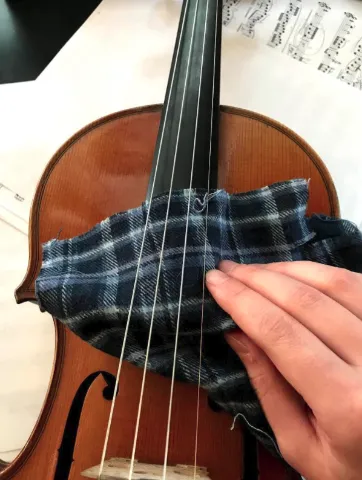 A person cleaning the violin fingerboard with a cloth.