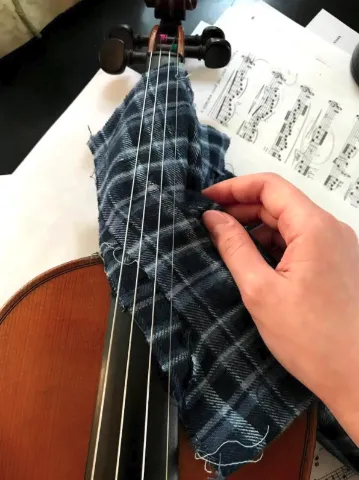 A person sliding a cloth in between the strings and the fingerboard of the violin to clean it.