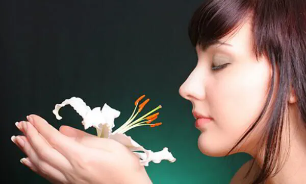 Woman smelling a white lily against a dark background.