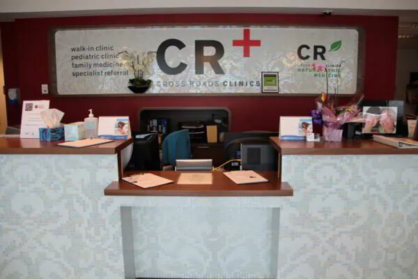 Reception area of Cross Roads Clinics with two desks, computers, and signage indicating medical services.