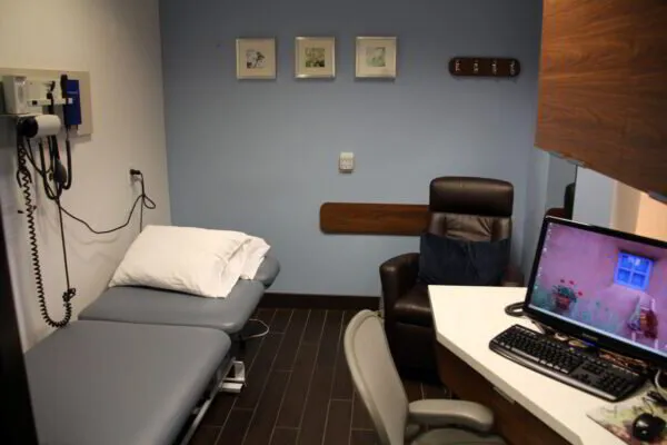 Modern doctor's office with an examination table, a chair, medical equipment, and a computer desk.
