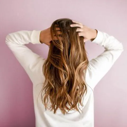 Woman with long wavy hair touching her head against a pink background.