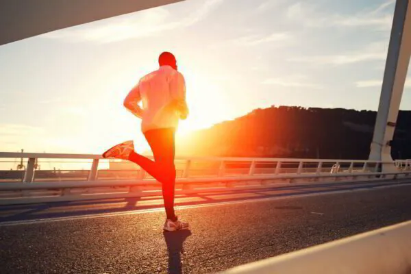 Person jogging on a bridge at sunrise with clear skies.