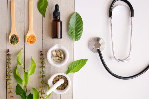 Herbal supplements and a stethoscope on a wooden surface, depicting traditional and modern medicine.