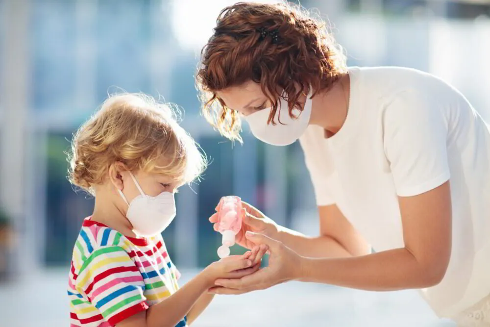 Woman in a mask giving hand sanitizer to a child outdoors.