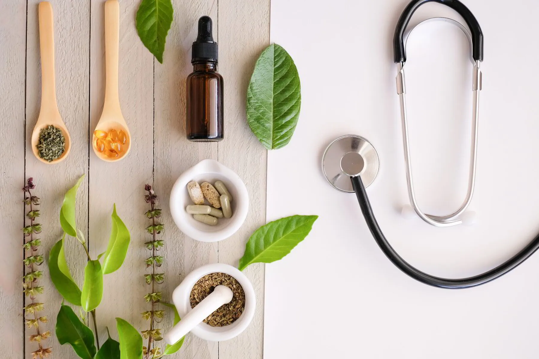 Herbal supplements and a stethoscope on a split white and wooden background, representing alternative and conventional medicine.