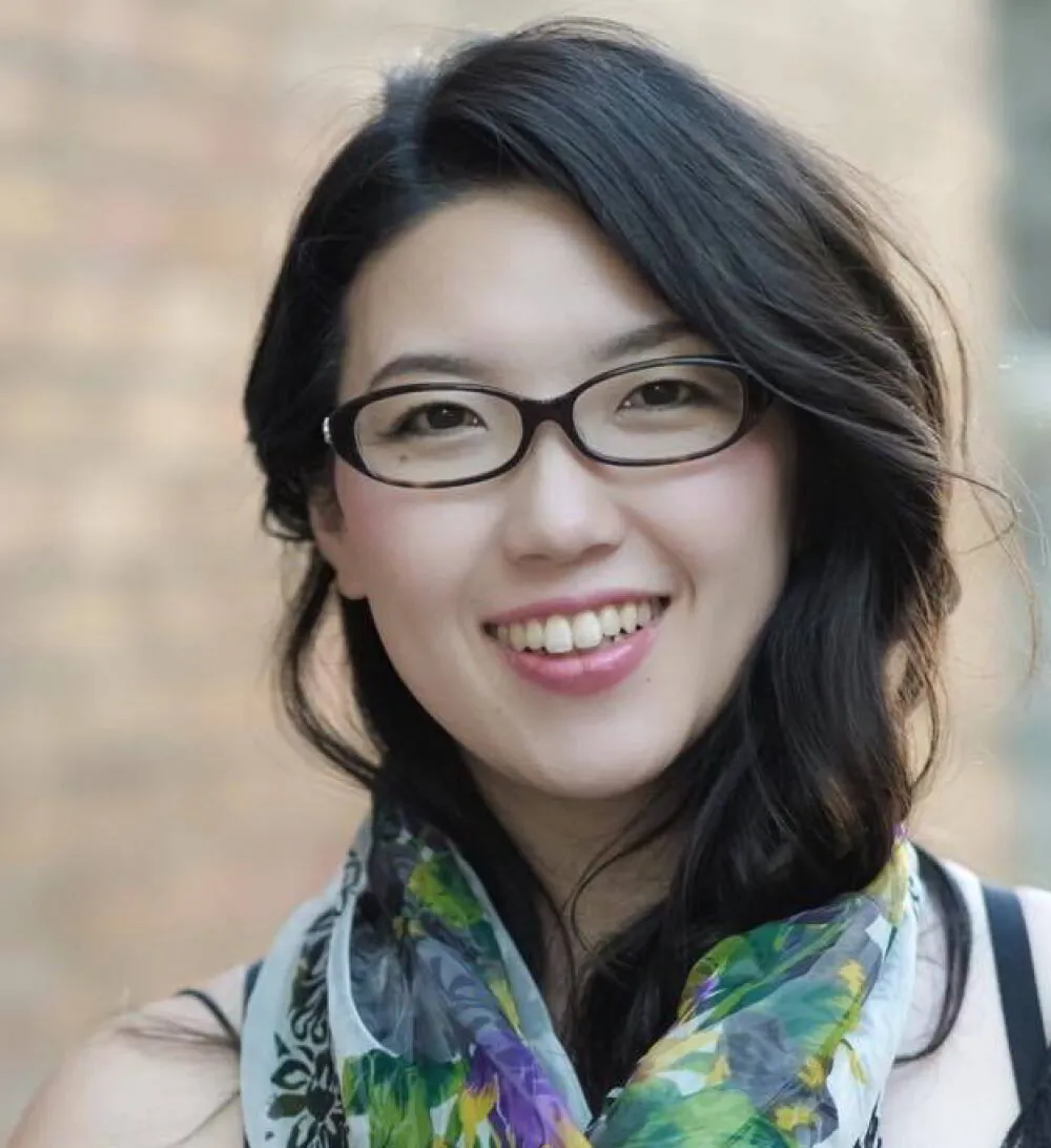 Smiling woman with glasses and a colorful scarf outdoors.