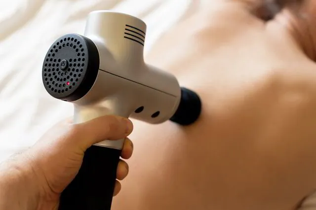 person with massage gun pressed to middle back