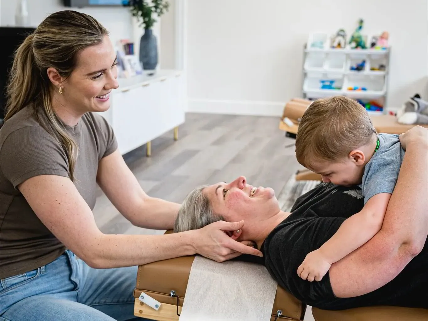 A mom being adjusted while her toddler hugs her, with the play area behind
