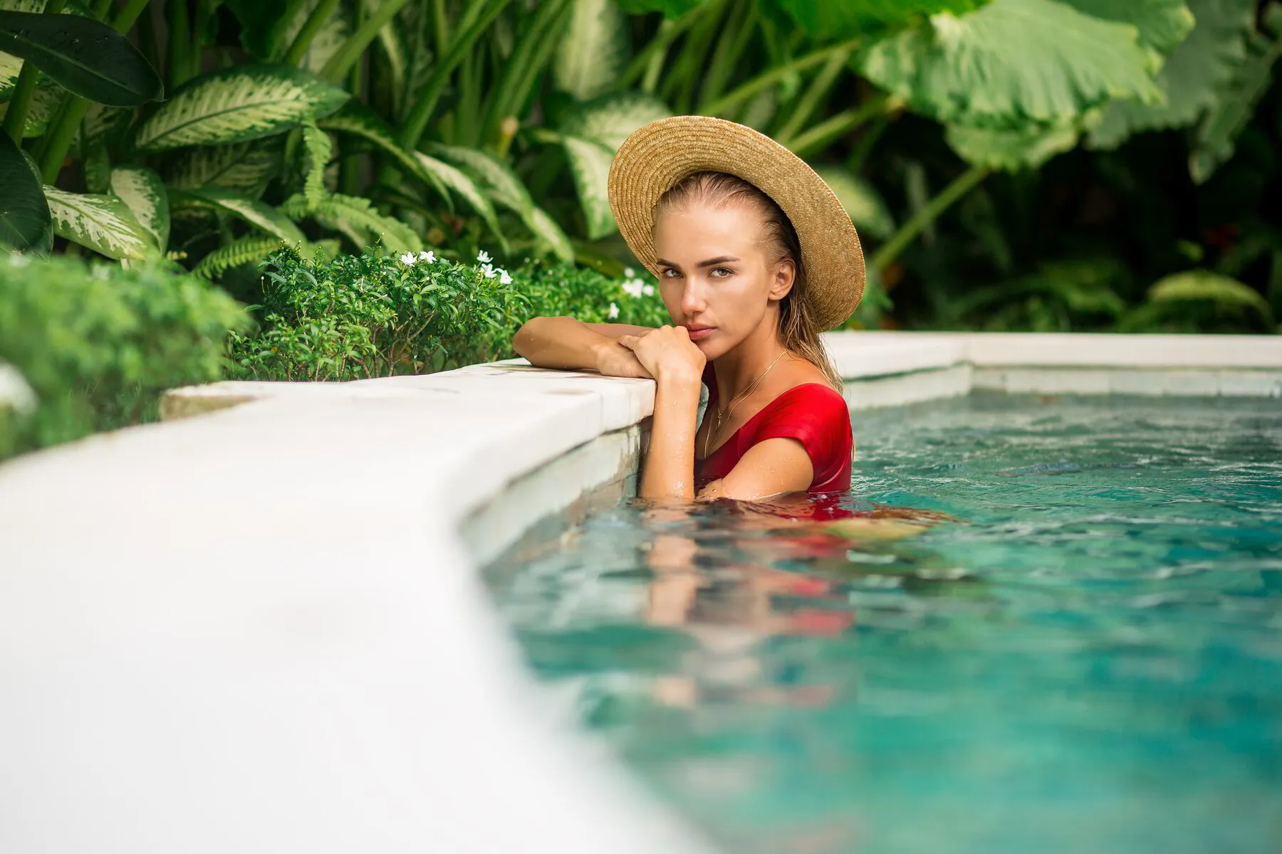 Living Pools & Spas. Blonde woman swimming in luxury pool leaning against pool wall near bushes and flowers