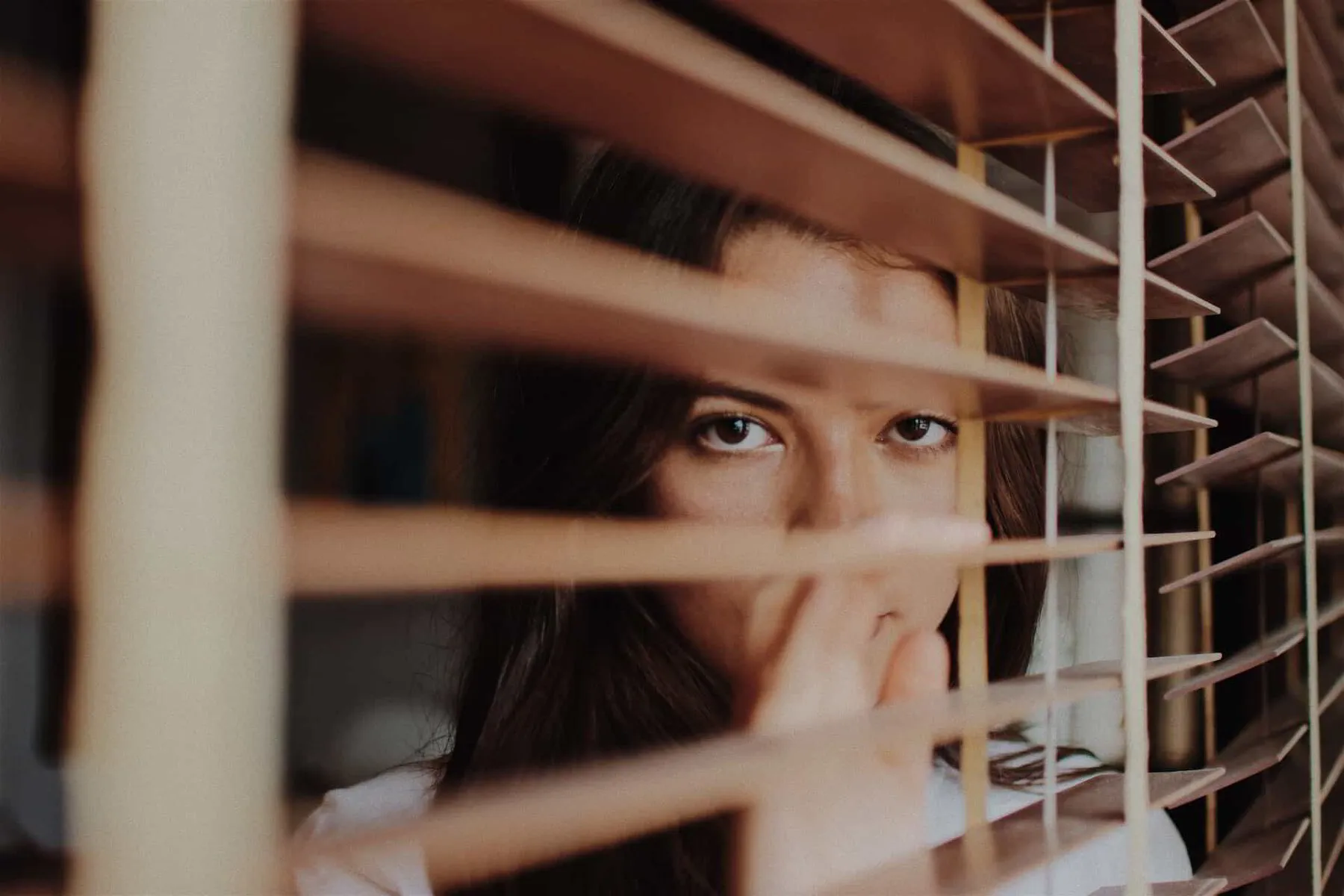 woman staring out of wood blinds
