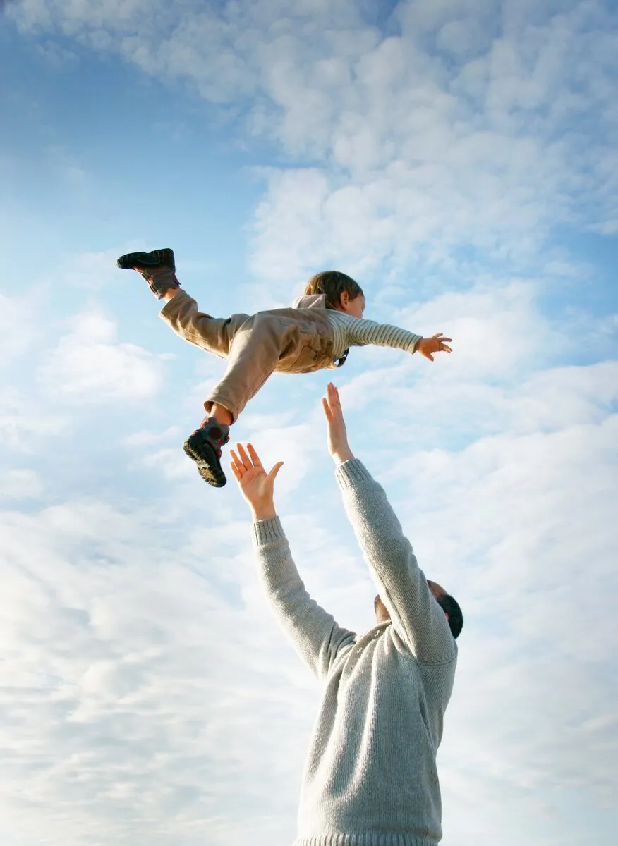Padre despreocupado lanzando alegremente al niño al aire, confiado en el futuro seguro del niño con IUL para Niños.