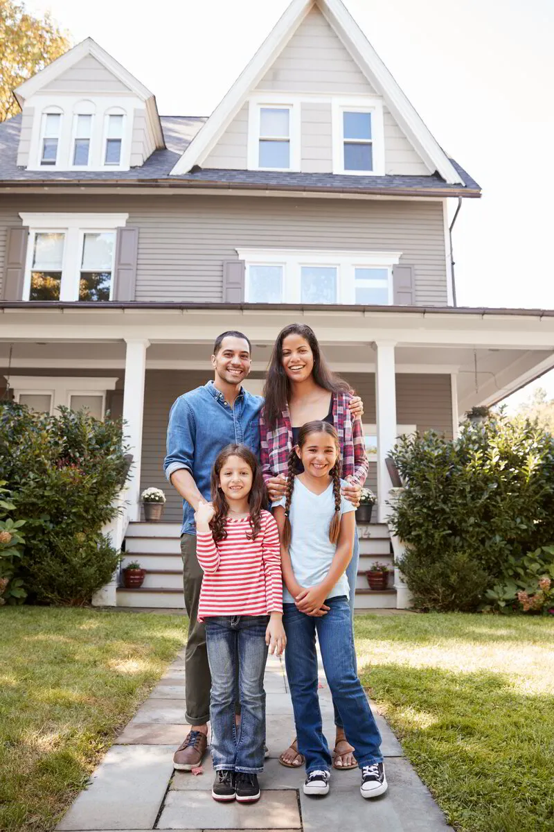 Familia de pie con orgullo frente a su hogar, seguros con su póliza de protección hipotecaria.