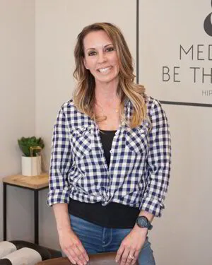 Woman in plaid shirt smiling in an office with motivational wall art.