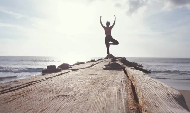 Person in yoga pose on a wooden pier by the sea at sunrise.