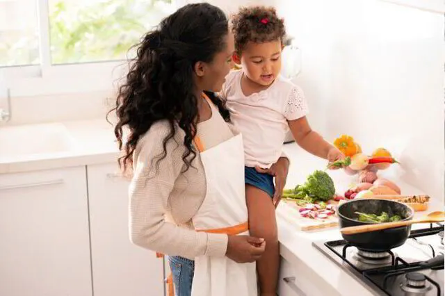 Mother and child preparing vegetables in a sunny kitchen.