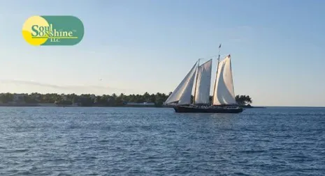 A sailboat with tall white sails glides across calm blue waters under a clear sky, with a small island and palm trees visible in the distance. The Soul Sonshine LLC logo appears in the upper left corner. The image symbolizes peace, direction, and the steady guidance of faith-led journeys. Meta Keywords: sailboat on ocean, Soul Sonshine LLC, faith journey, peaceful waters, sailing toward purpose, Christian publishing, inspirational voyage, calm seas.
