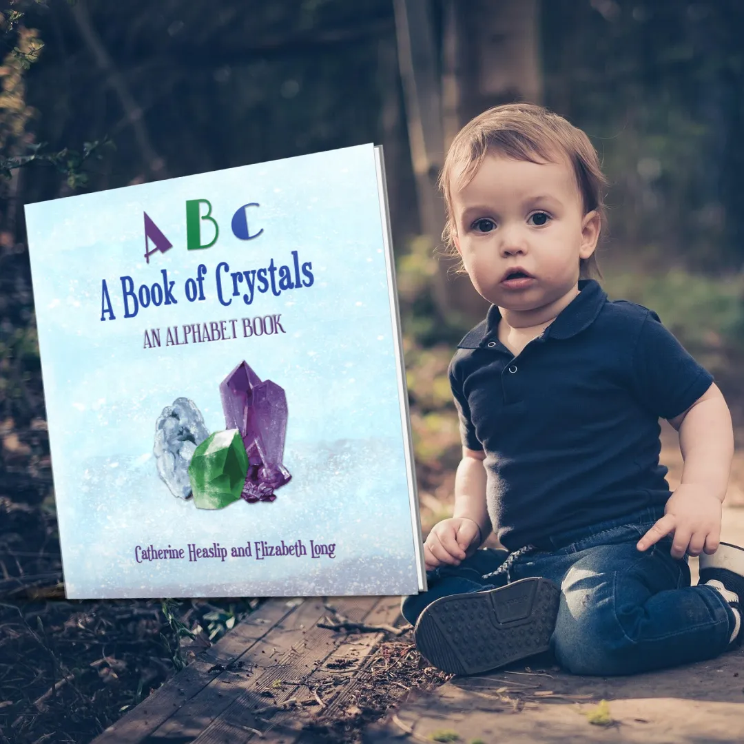 Book cover for ABC: A Book of Crystals – An Alphabet Book by Catherine Heaslip and Elizabeth Long. The cover features three sparkling crystals — a green emerald, a purple amethyst, and a blue quartz — resting on an icy blue surface. The title letters “A,” “B,” and “C” are each in different colors above the subtitle. A gold banner in the top left corner reads “#1 Best Seller.” The border is a vivid blend of rainbow colors, giving the design an energetic and educational feel.
