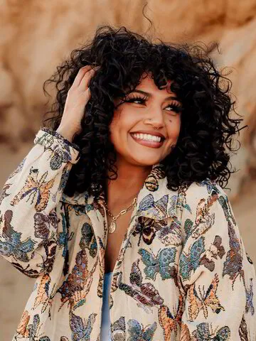 Lizette Aleman, a stylist with a radiant smile at Midtown Curls, adorned with fun hair buns, represents the creative and welcoming atmosphere of the Reno, NV salon.