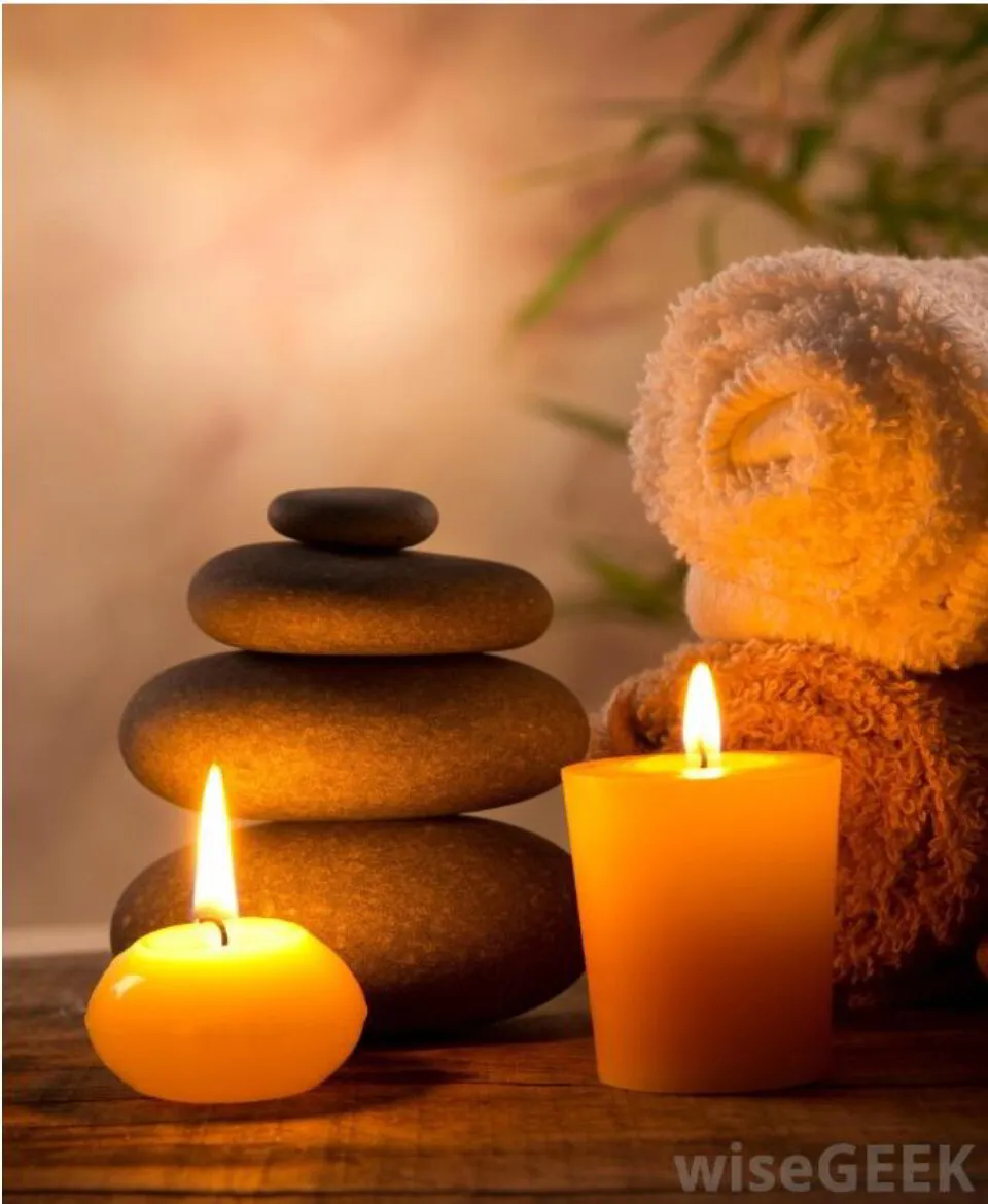 relaxing spa image with lit candles next to smooth stones and soft towels 