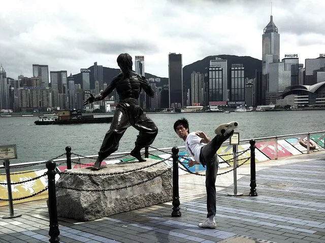 Albert Chan performing a side kick next to the Bruce Lee statue in Hong Kong