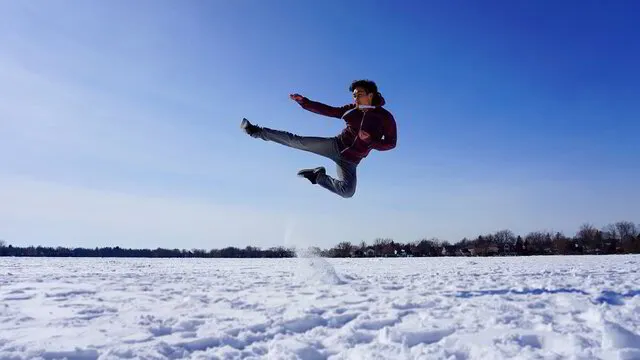 Albert Chan performing a flying side kick in the snow in Canada