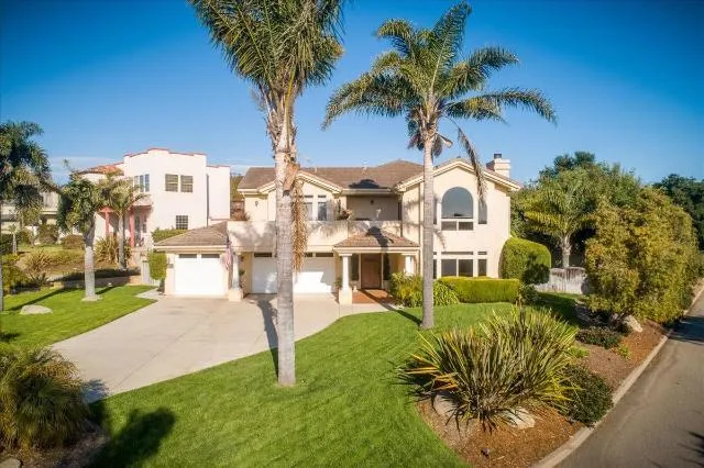 Photo of large house, blue sky background, with palm trees and green lawn with tidy landscaping.
