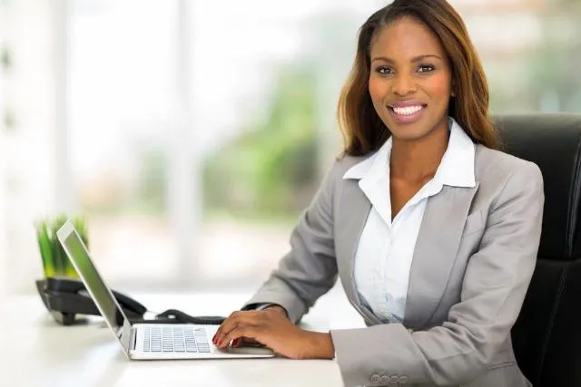 Female real estate agent smiling working at her desk on laptop computer